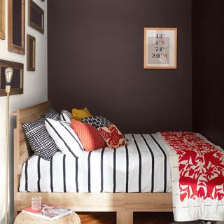 A small bedroom with a wooden bed with mixmatched bedding with the walls painted in Etiquette and Wenge shades