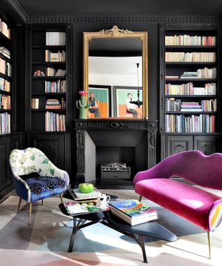 A black living room with built-in alcove bookcases either side of a black fireplace pink and a mid-century pink sofa.