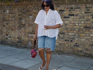 Chiara wears an oversize white short-sleeve button-down, long denim shorts, and silver thong heels