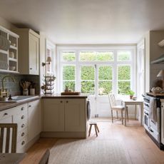 country-style kitchen with cream shaker units and range cooker, wooden floor and large windows at end of room