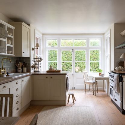 country-style kitchen with cream shaker units and range cooker, wooden floor and large windows at end of room