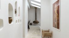 A white home with in-wall storage shelves, an oval ceiling fireplace, a framed art piece and a stone floor 