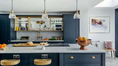 Kitchen island with dark blue kitchen units, grey marbled worktop and splash back. A period village house with a contemporary glass extension and modern interior
