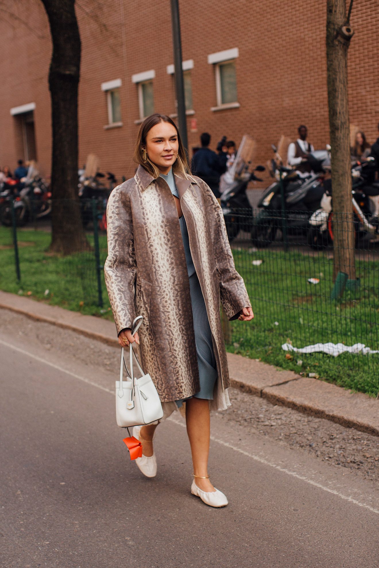 fashion week attendee wearing printed coat, white handbag, and white ballet flats