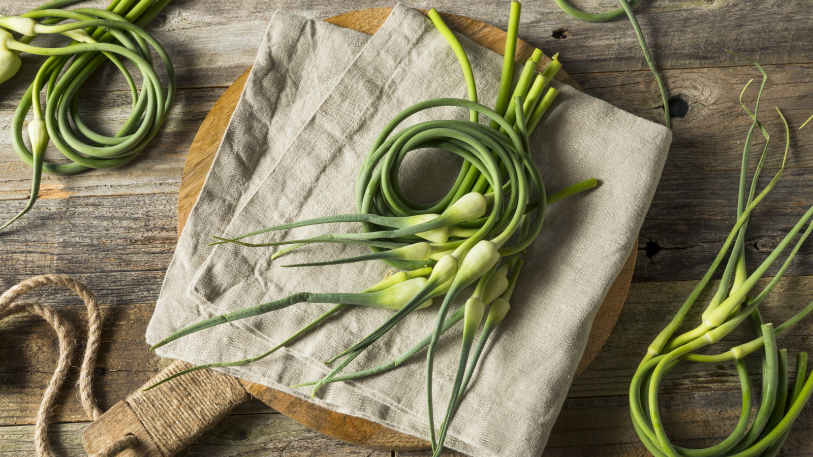 Raw green garlic scapes on a wooden chopping board