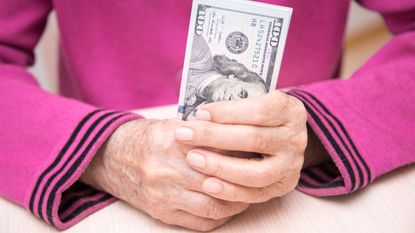 An older woman holds a stack of cash in her hands.