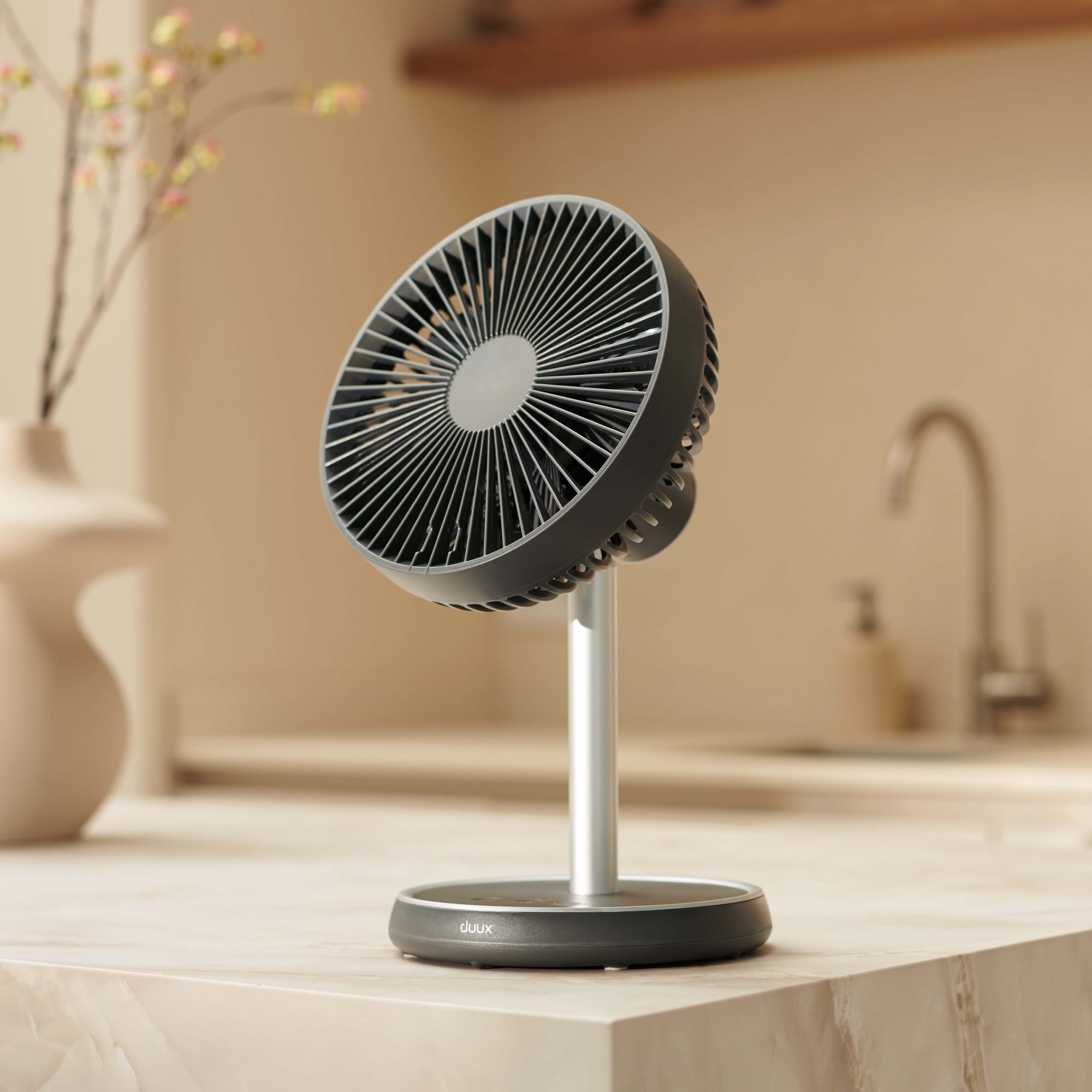 Charcoal grey Duux Rize fan in desktop configuration on a marble kitchen island in a neutral kitchen