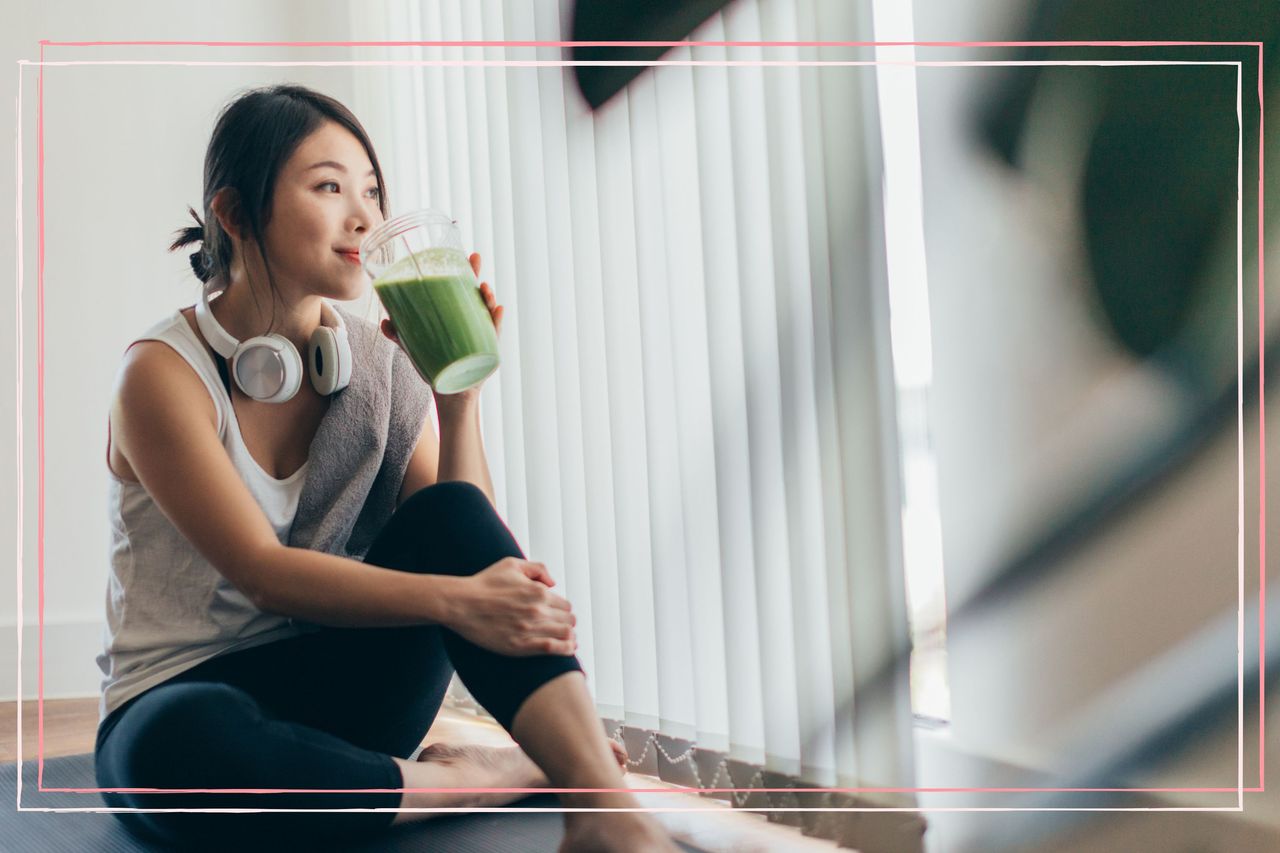 A woman in workout gear sat on the floor drinking a green smoothie