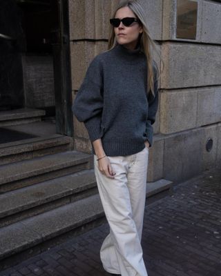 Model and fashion influencer Linda Tol on the street in Europe wearing a chic fall outfit styled with white jeans.