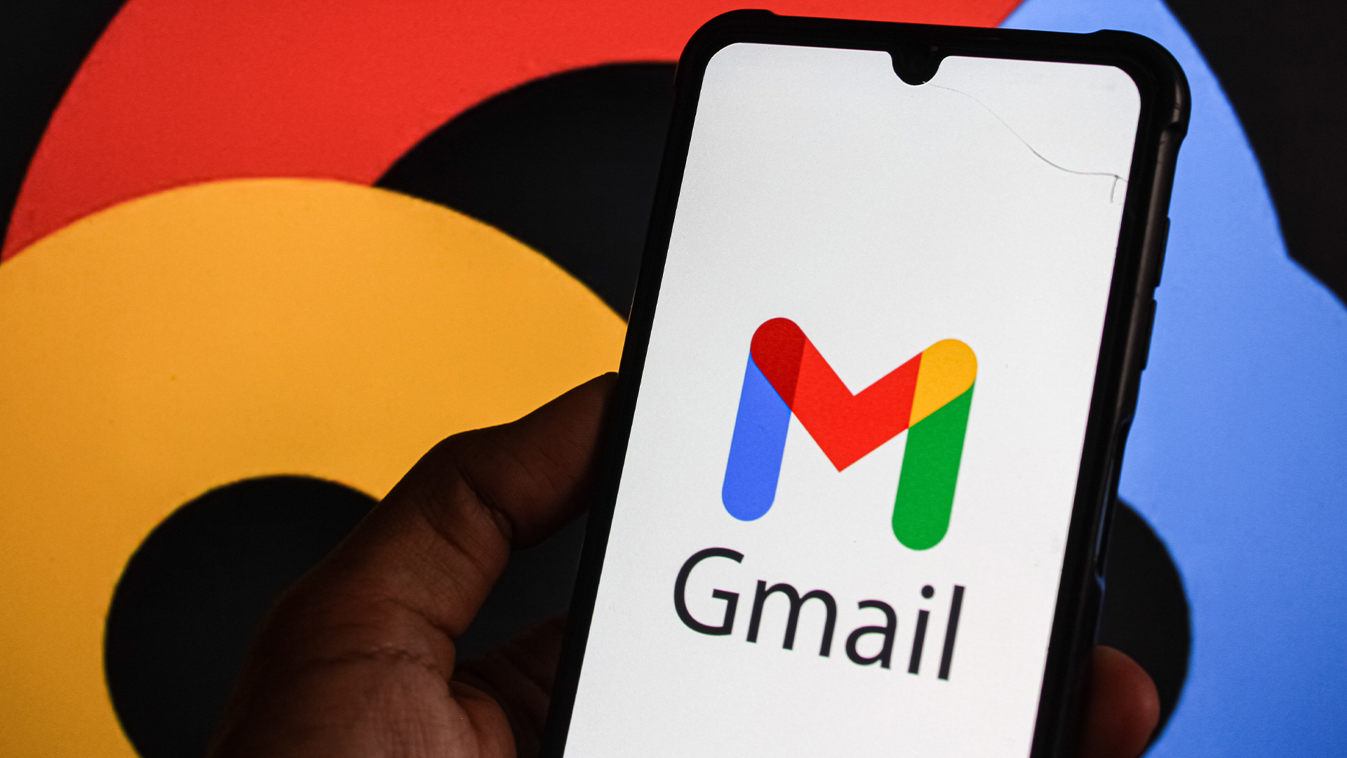 Gmail logo and branding pictured on a smartphone screen with company colors and branding also pictured in background.