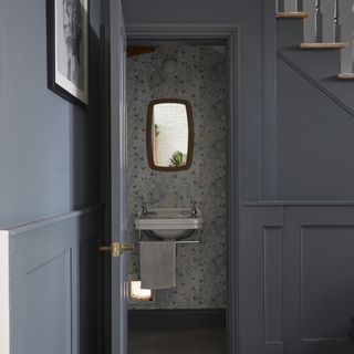 downstairs toilet under the stairs with wallpaper and wood mirror