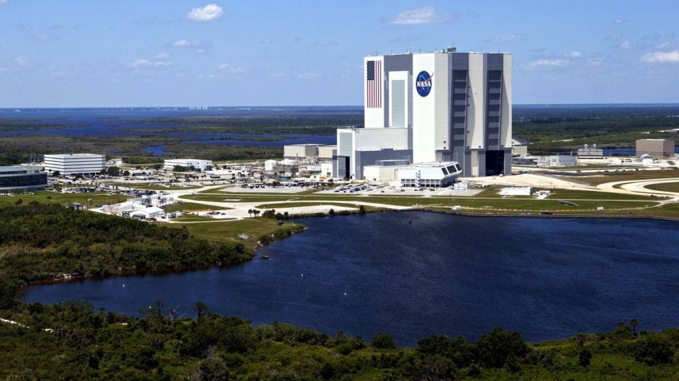 photo of a large white building with an american flag and the nasa logo painted on its outside next to a large lake