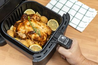 Hand holding air fryer cooking a whole roasted chicken.