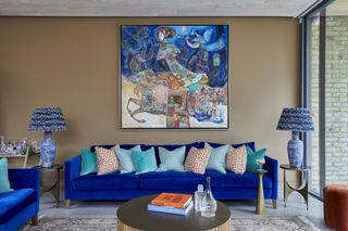 A royal blue sofa stands out against a taupe wall