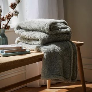 A sage green fluffy blanket on a wooden bench seat