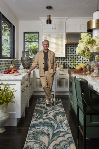 martyn lawrence bullard in a kitchen with his ruggable collection, flowers on counter, and mosaic tile backsplash