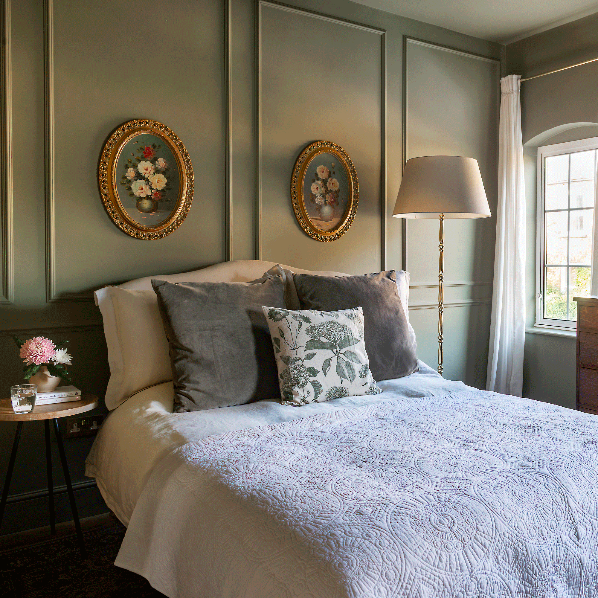 a bedroom with dark green wall panelling and two matching floral artworks on the wall