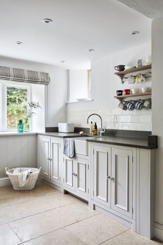 A bright utility room with a butlers sink and black stone worktops.