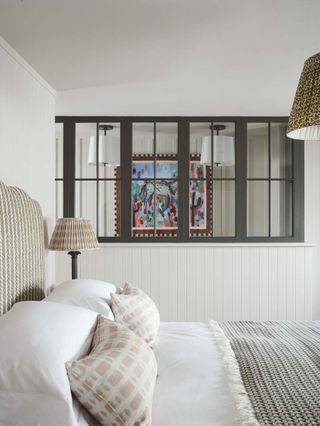 A bedroom with white shiplap walls and an internal window