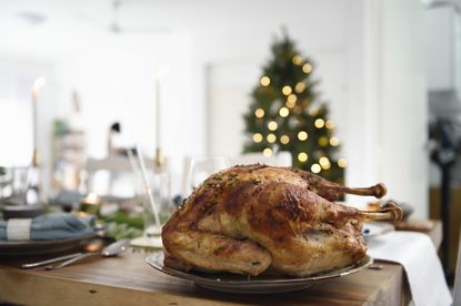 Roast turkey on a table laid for dinner with a Christmas tree in the background
