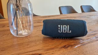 JBL Charge 5 Bluetooth Lautsprecher auf einem Holztisch neben einer Blumenvase