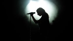 a dramatically-lit photograph showing the silhouette of a woman with a microphone