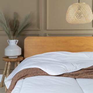 Bed with wooden headboard and white duvet under rattan lampshade