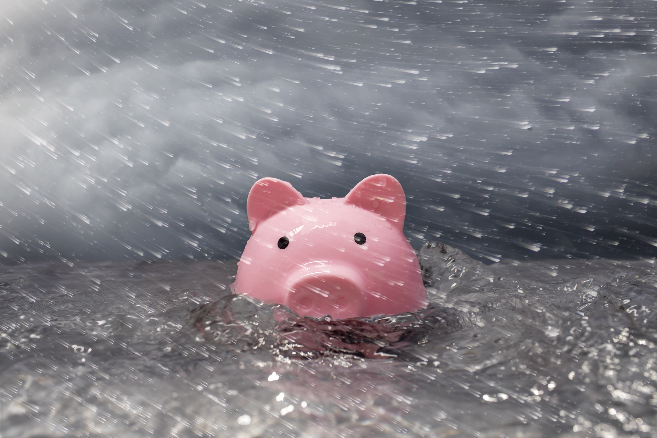 Pink piggy bank partially submerged in turbulent water, stormy sky, wind blown rain