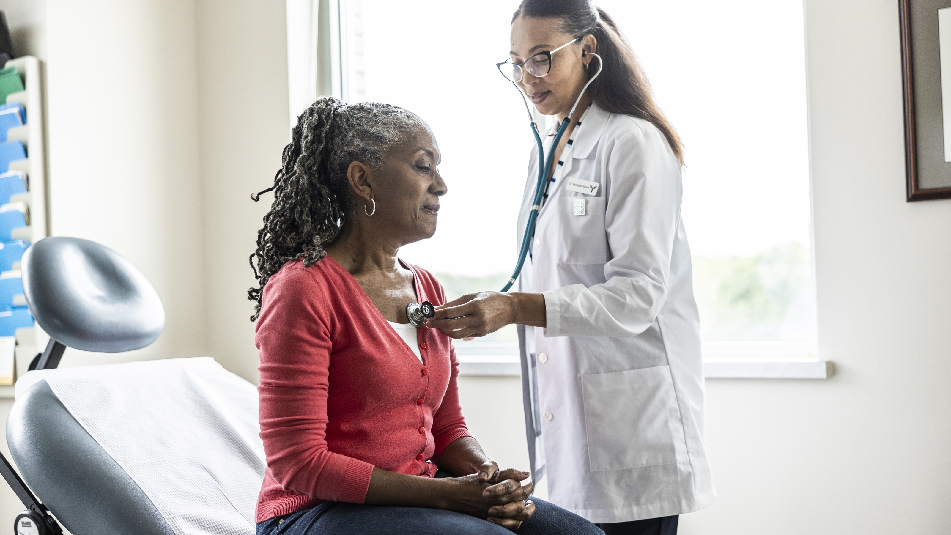 A doctor uses her stethoscope to listen to an older woman's heart in a doctor's office. 