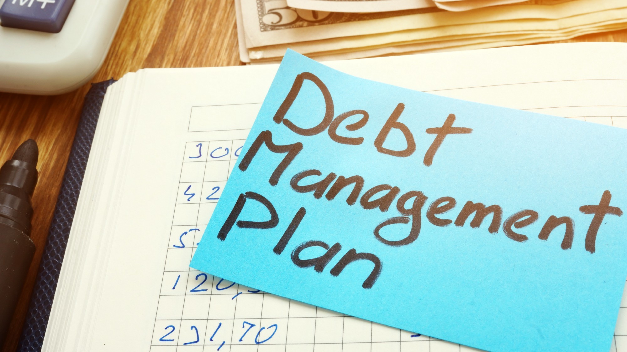 A blue sticky note that reads "Debt management plan" next to a calculator and cash
