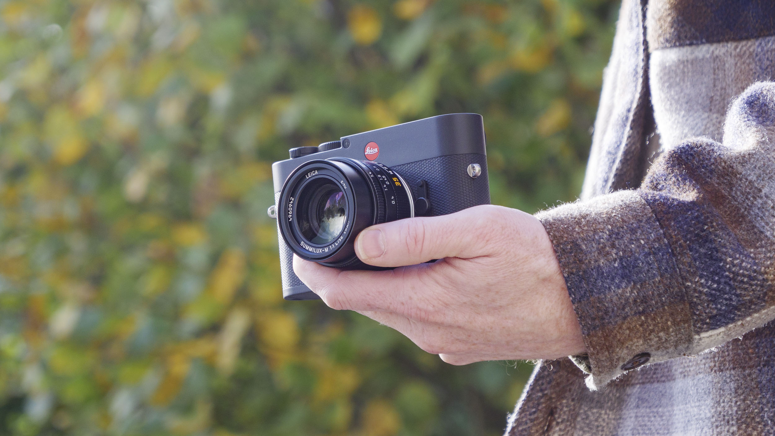 Leica M EV1 camera in user's hands, autumn leaf backdrop