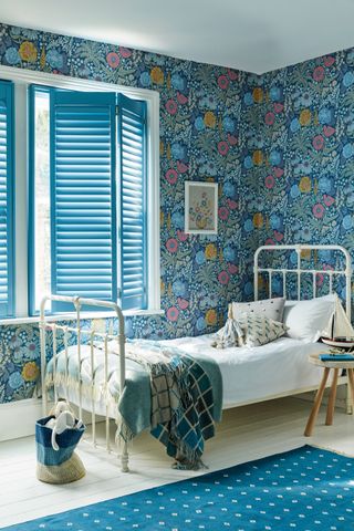 blue toned floral wallpapered bedroom complete with industrial style white metal bed