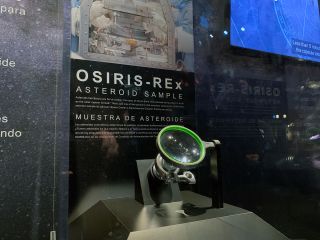 closeup of a glass display case in a museum showing a small asteroid sample returned to earth by nasa's osiris-rex mission