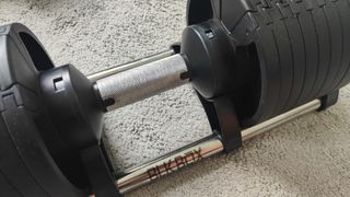 Closeup of the BLK BOX Adjustable Dumbbell on a carpeted floor