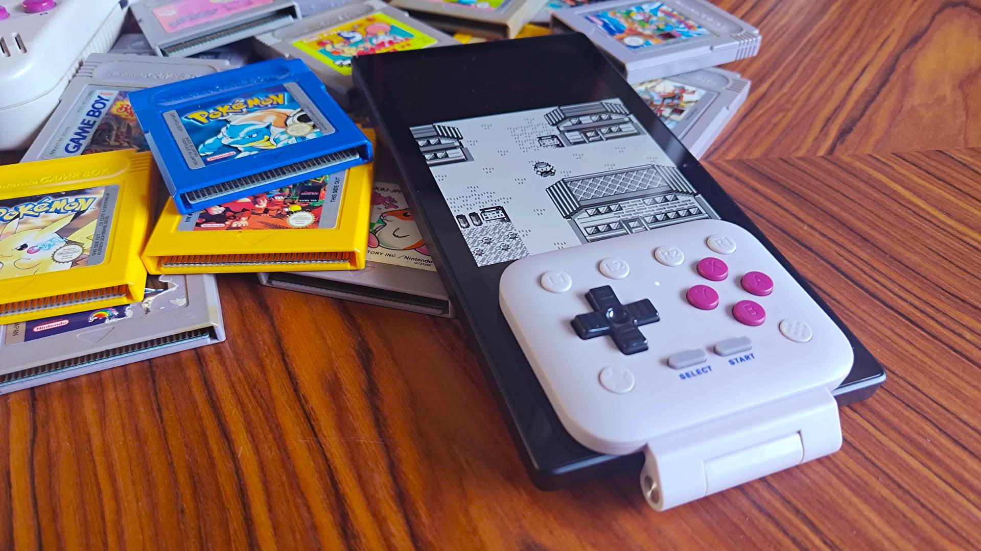 Razer Edge connected to 8Bitdo FlipPad lying next to Game Boy cartridges on woodgrain table.