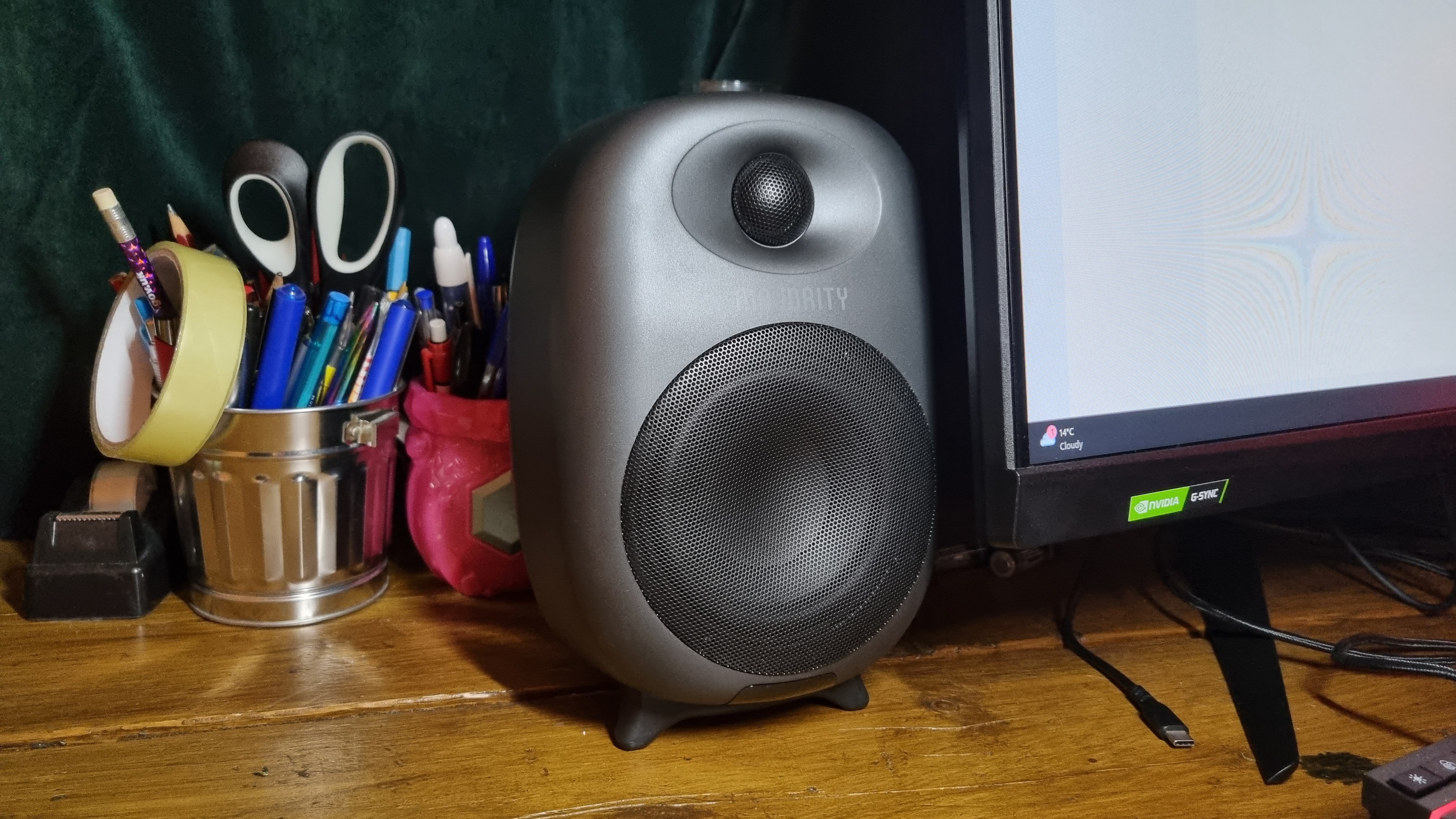 One of the Majority D80 speakers next to a 32-inch computer monitor, with pots of pens and scissors for scale