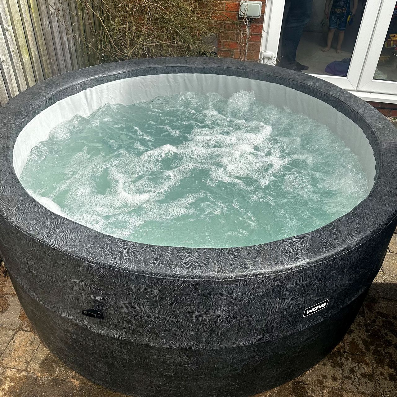The grey Wave Osaka hot tub filled with bubbling blue water in a garden