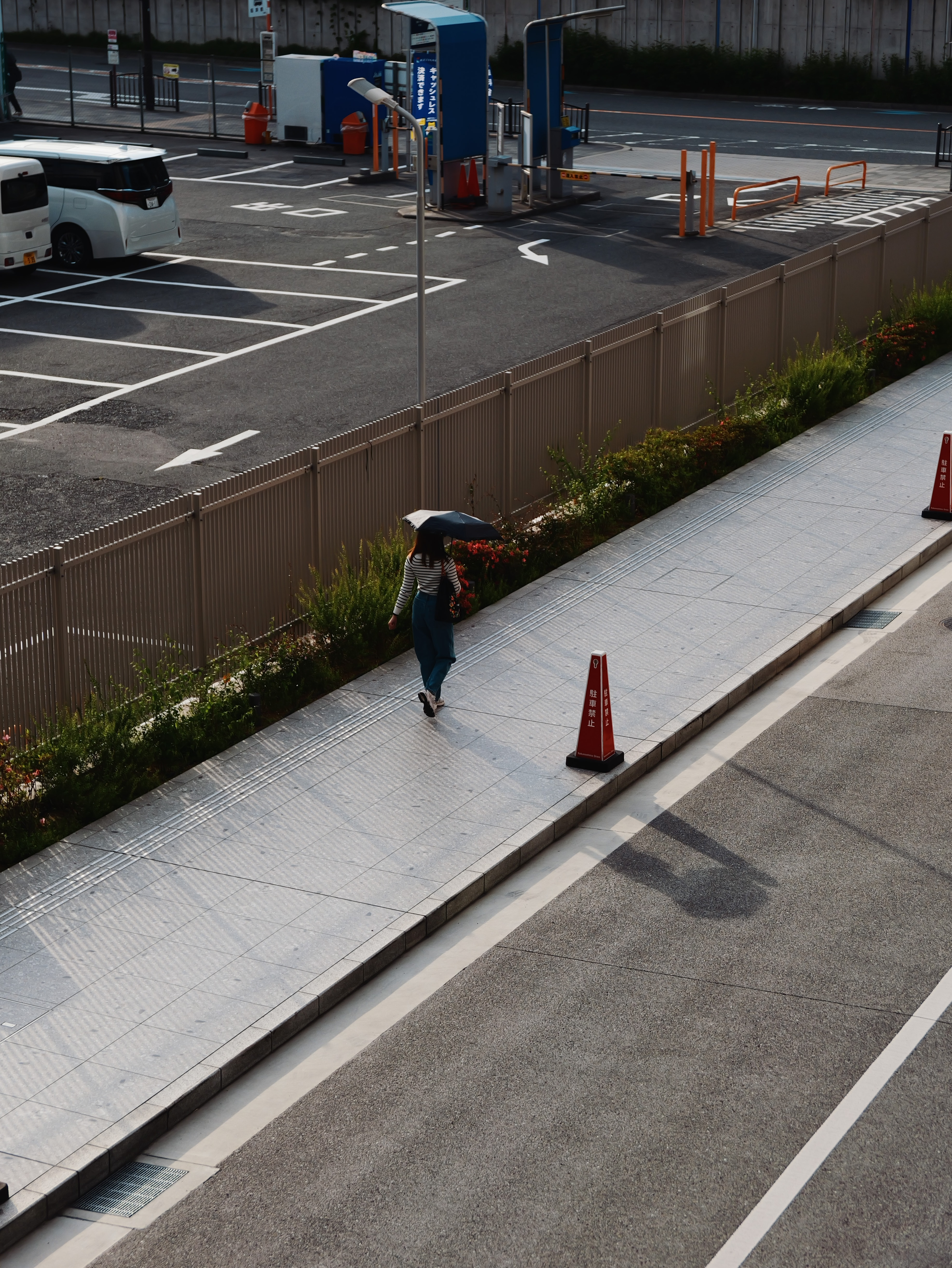 Person with an umbrella walking along a sunny city sidewalk.