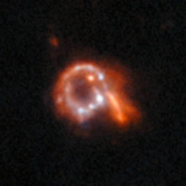 A small image of a mostly red galaxy. Unusually, it is ring-shaped with spots of light around the ring, a protruding arm on one side and a dark hole in the centre.