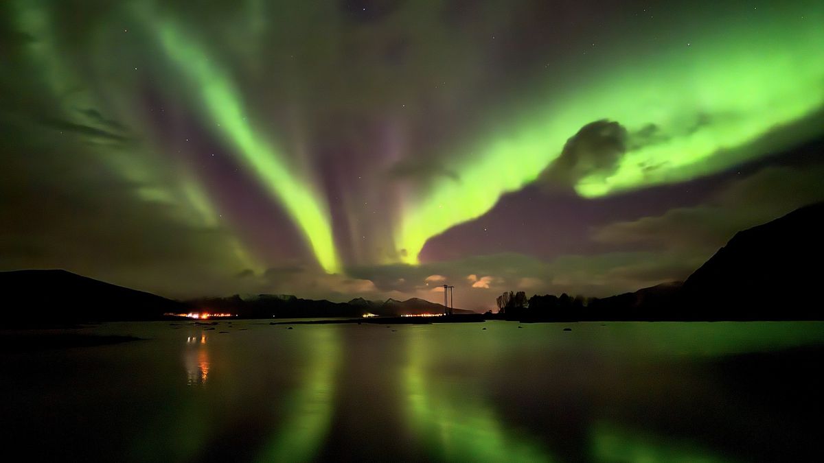 green northern lights reflect in the water below and look like butterfly wings.