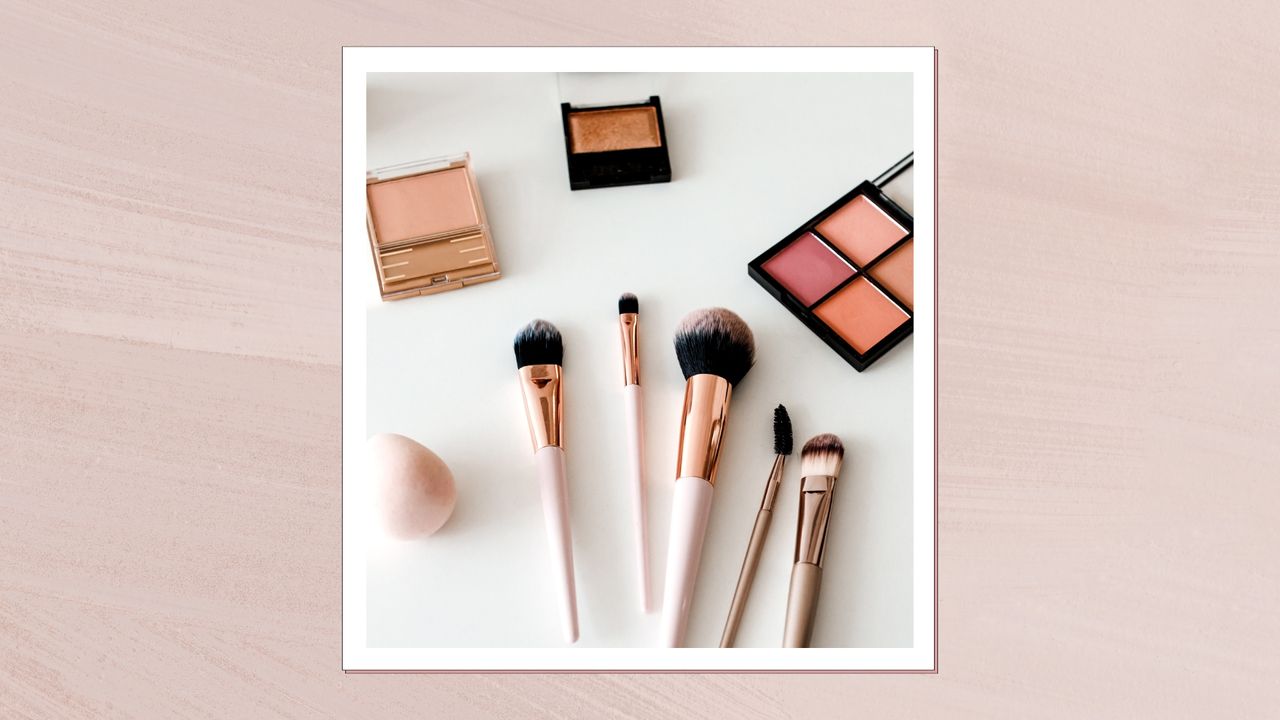 A collection of makeup brushes, a makeup sponge and makeup palettes laid out on a white background/ and pictured in a pink template