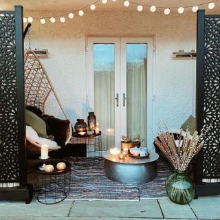 A hammock, black Moroccan-style screens, and varies side tables on top of a rug, in a small garden