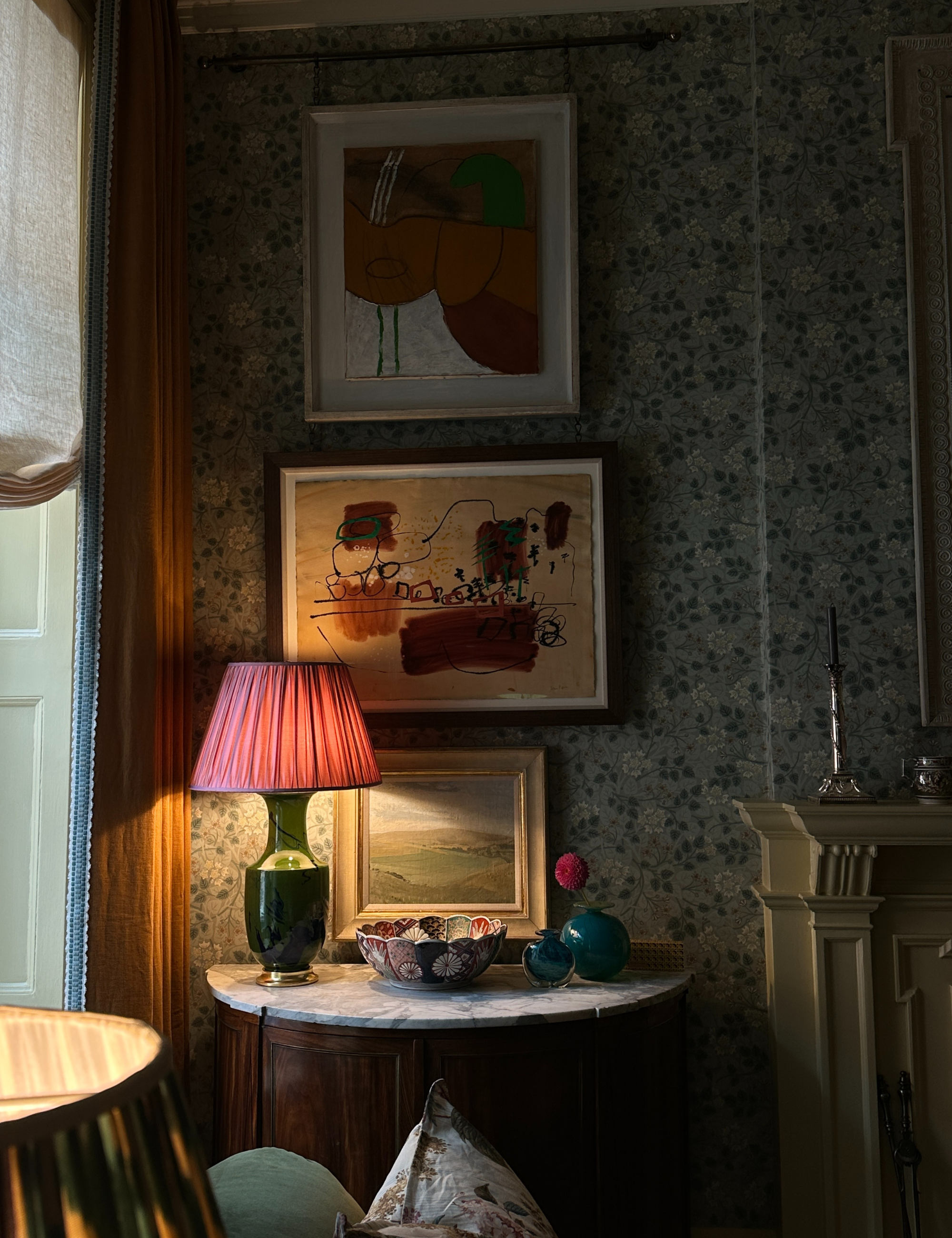 Pink and green table lamp pictured inside of a dimly lit, collected living room