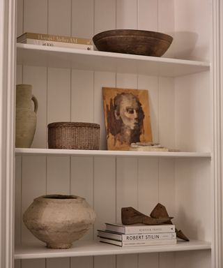 A white paneled bookshelf with two stacks of books, a piece of art, and decorative objects