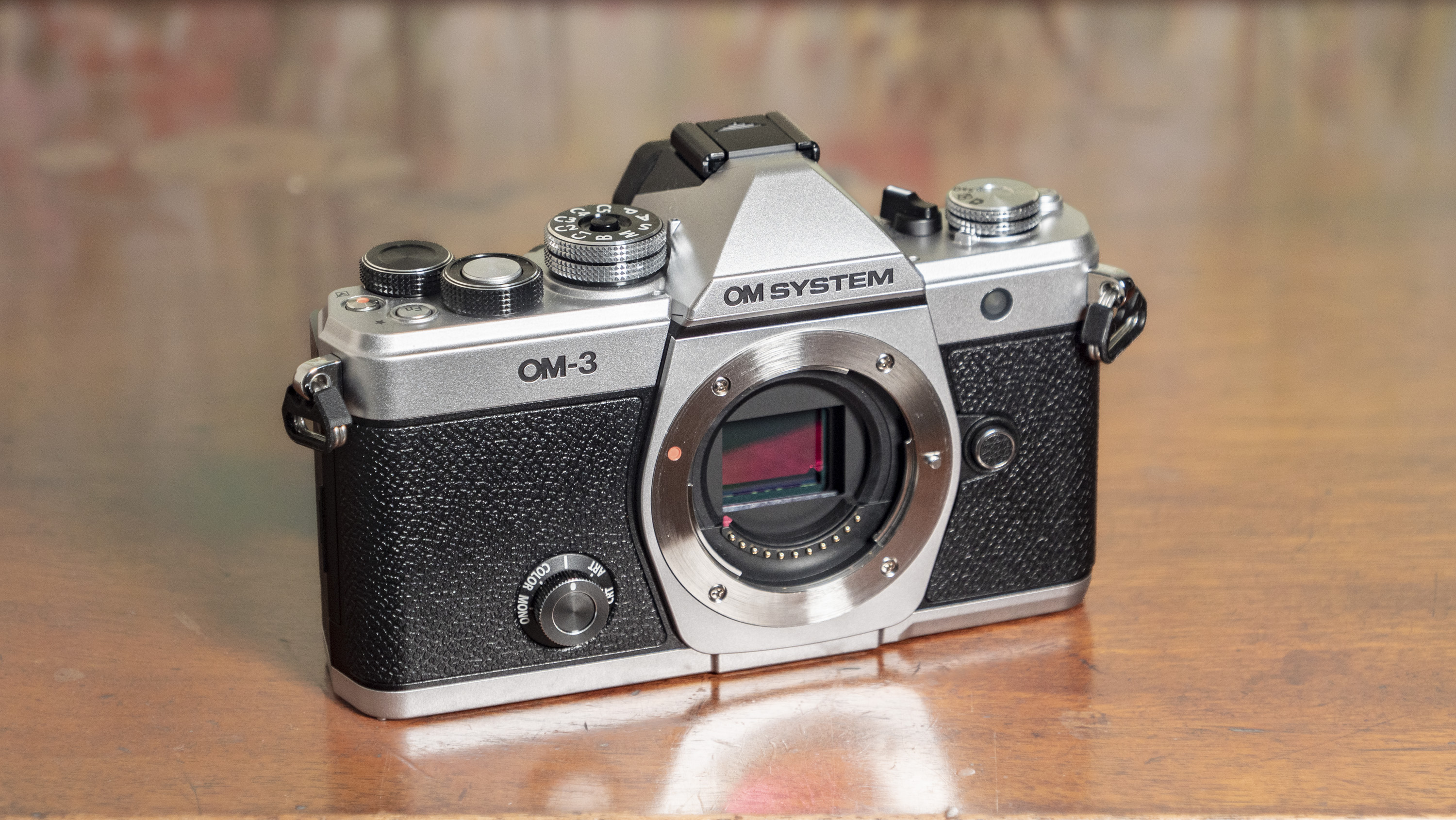 OM System OM-3 mirrorless camera on a wooden surface, no lens attached