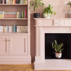 A colour-drenched pink living room with a fireplace and a bookcase