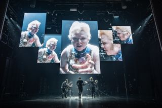 sarah snook starring in the picture of dorian gray on broadway as an image of her in a blonde wig is projected on multiple screens while a camera crew surrounds her