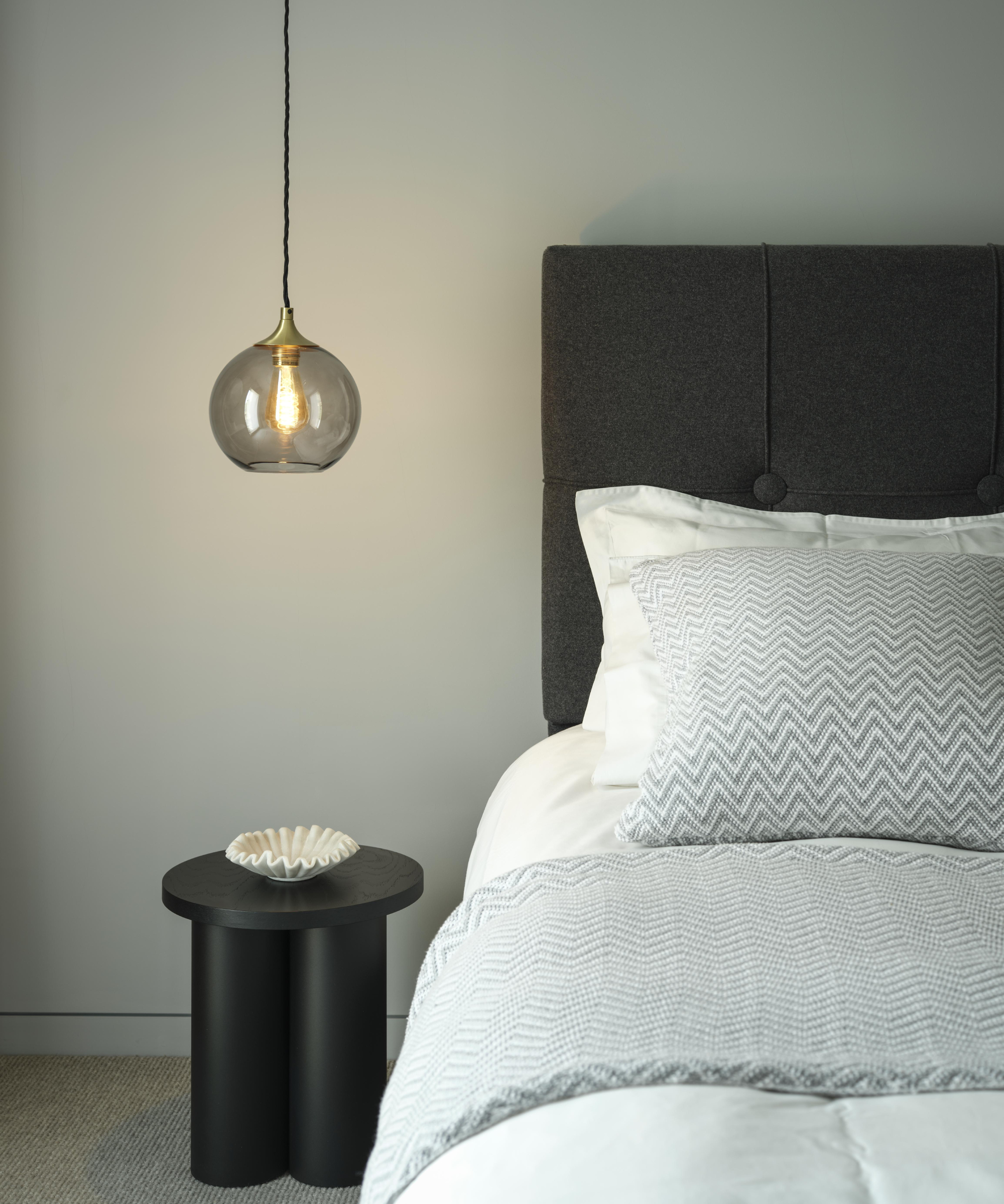 bedroom with small smoked glass pendant light having over small black table to side of bed