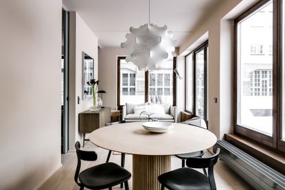 Room with round table and chairs and a white lamp hanging over it, a couch against the wall and large windows 