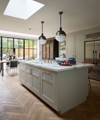 An open-plan kitchen with herringbone flooring and a large kitchen island with pendant lights above it
